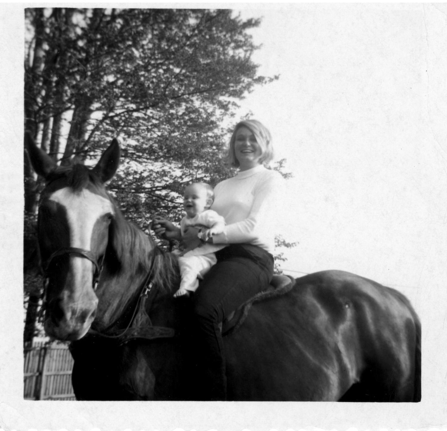 A black and white photo of Bonnie holding a baby Devon on a horse together