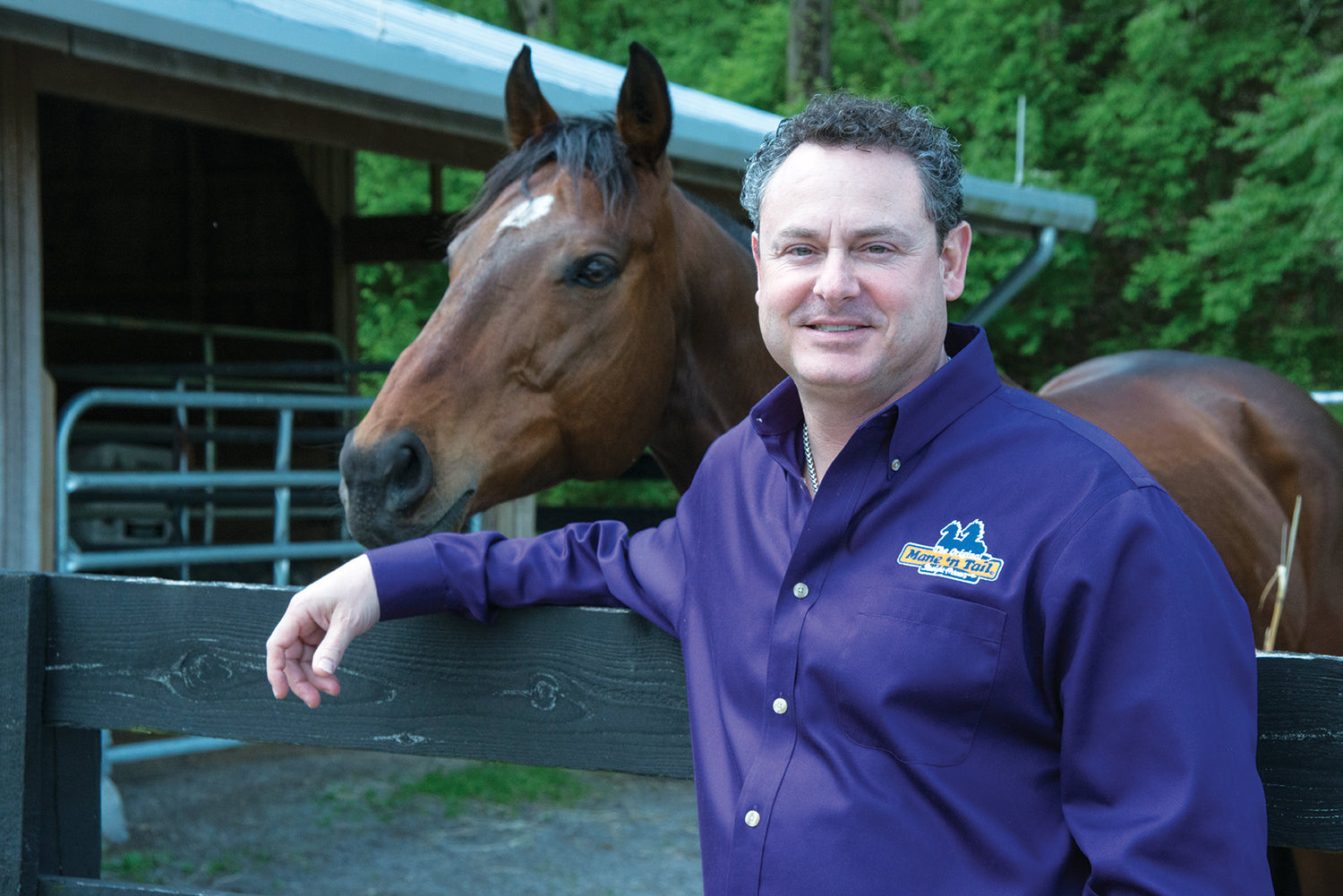 Devon Katzev standing in front of a horse in a Mane 'n Tail embroidered blue dress shirt.