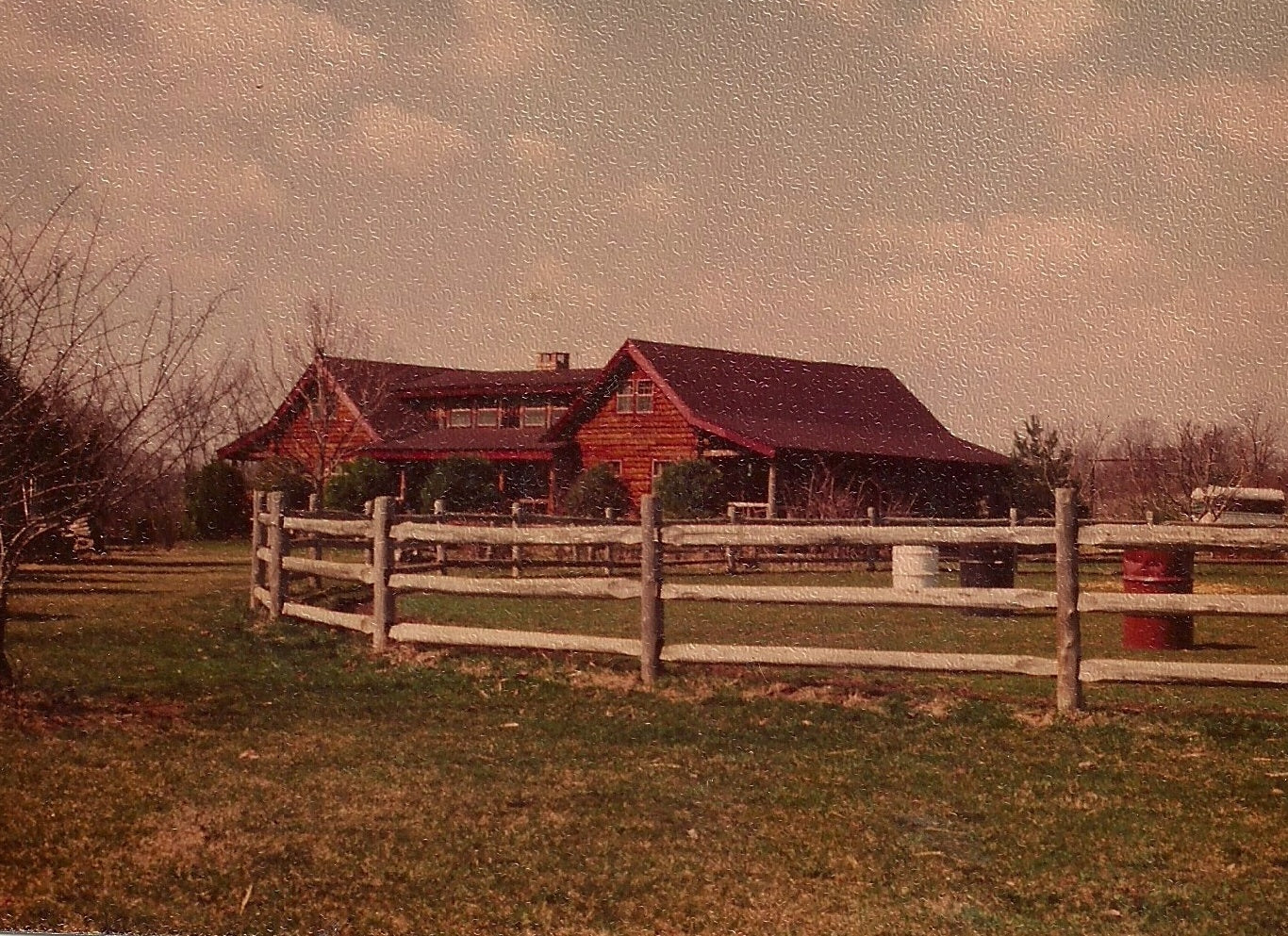 A texture photo of the Katzev family farm. There is a fence on the forefront that have barrels in the middle as obstacles