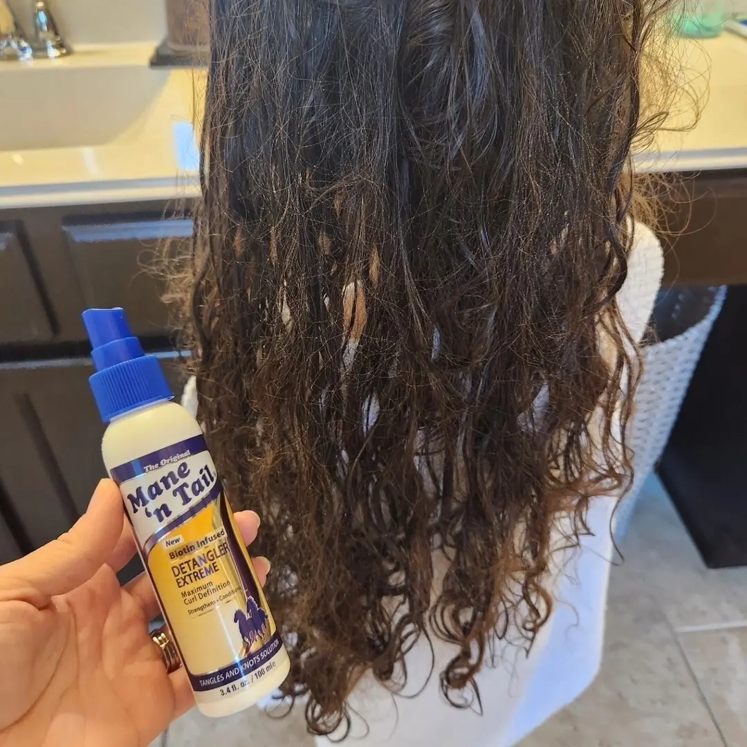 This is a photo of a girl with wavy knotted hair. There is a hand holding Mane 'n Tail Detangler Extreme.